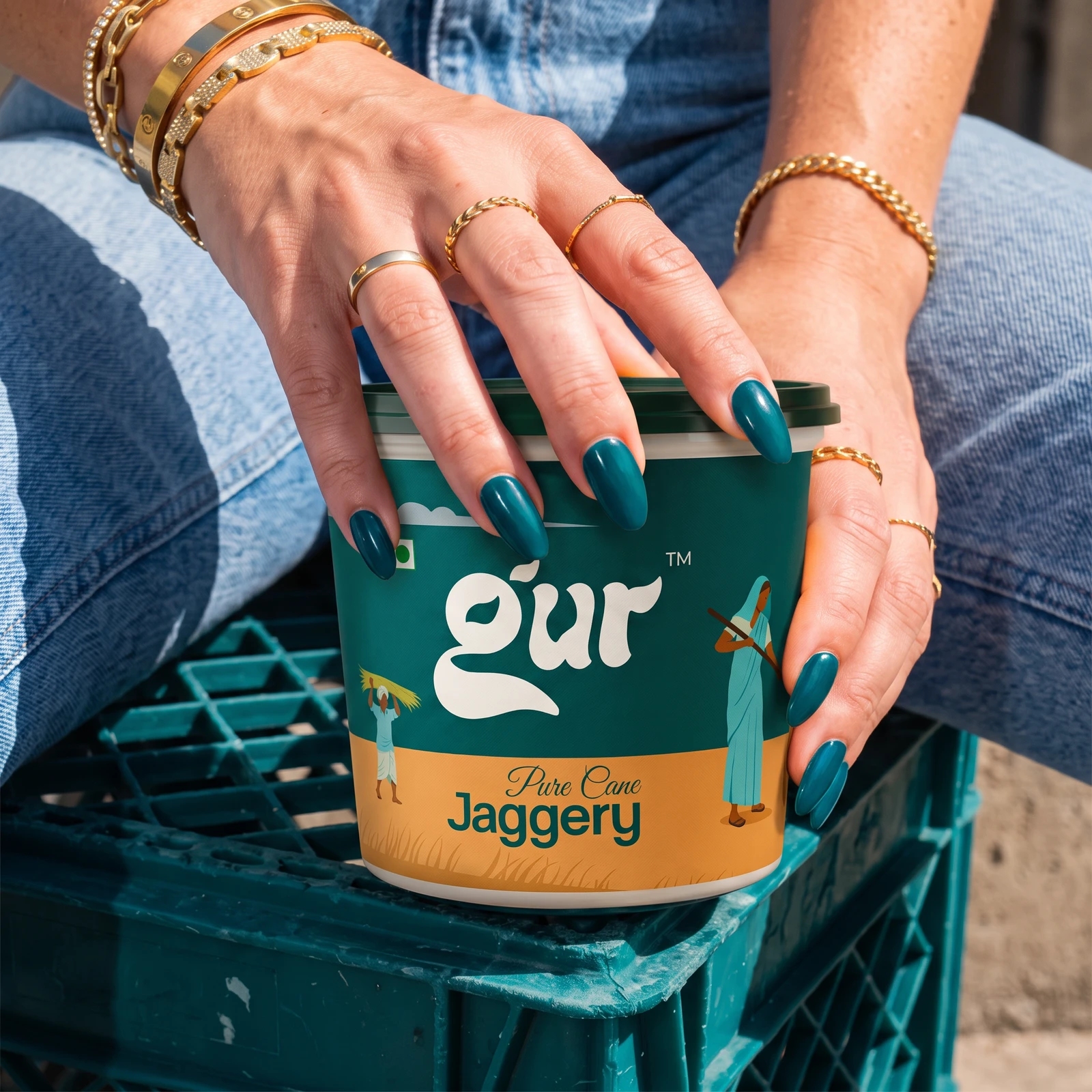 Hand with teal nails and gold jewellery resting on the GUR tub, on a matching teal crate